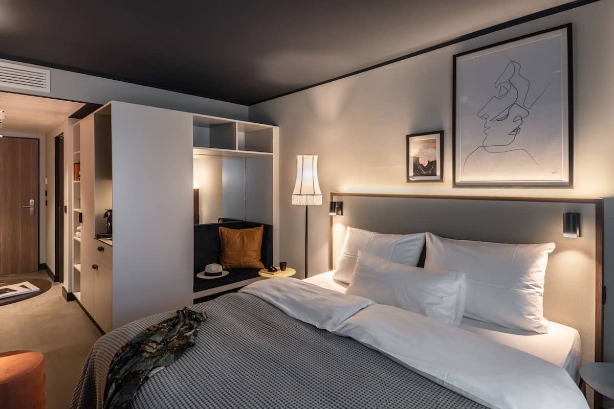 Una habitación de hotel moderna con una cama grande, una mesita de noche, un armario y una obra de arte enmarcada en la pared.
