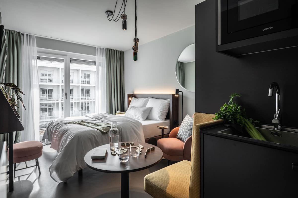 Habitación de hotel moderna con cama, mesita de noche y vista a un edificio a través de amplias ventanas.