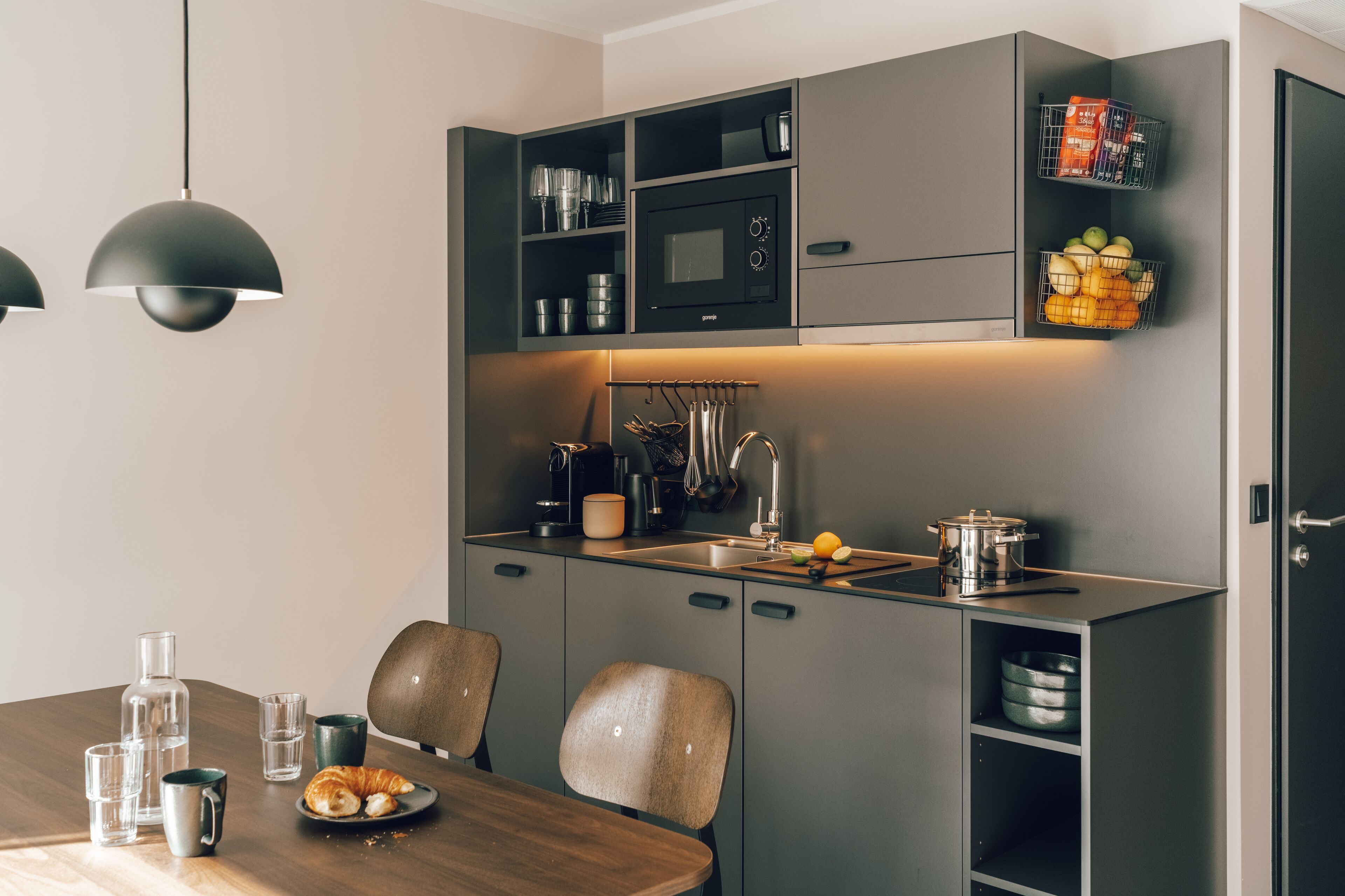 A modern kitchen with built-in appliances, a dining area with a wooden table and chairs, and a hanging light fixture.