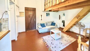 Ein großzügiger Wohnbereich mit einer Holztreppe, einem weißen Sofa, einem kleinen weißen Tisch und einem gemusterten Teppich.