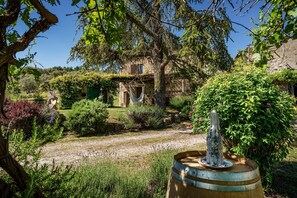 A rustic stone building with a garden, a hammock, and a fountain.