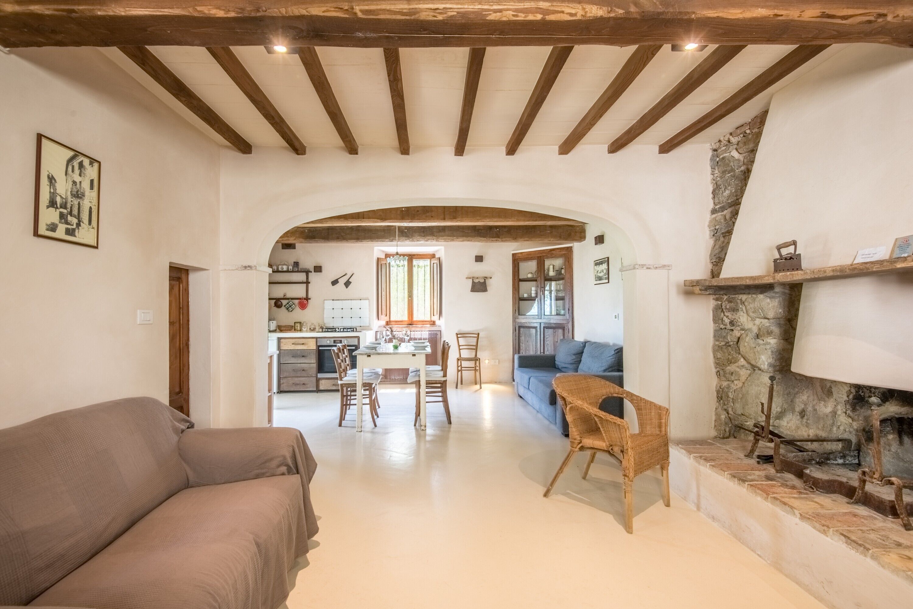 A spacious living area with a sofa, a dining table with chairs, a kitchen in the background, and a stone fireplace.