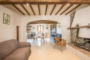Un vaste espace de vie comprenant un canapé, une table à manger avec des chaises, une cuisine à l’arrière-plan et une cheminée en pierre.