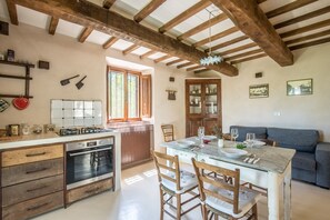 Une cuisine rustique avec des poutres en bois, un coin repas avec une table en verre et un canapé bleu.