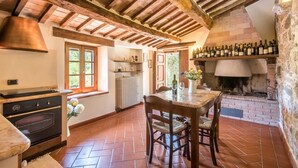 Cocina rústica con vigas de madera, chimenea de ladrillo y una mesa de comedor con sillas.