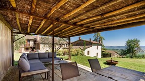 Un patio al aire libre con una mesa y sillas de madera, un sofá y una estructura de techo de paja.