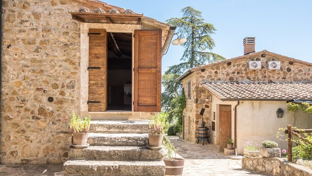 Un edificio de piedra con puerta de madera, escalones que conducen a un porche y plantas en macetas.