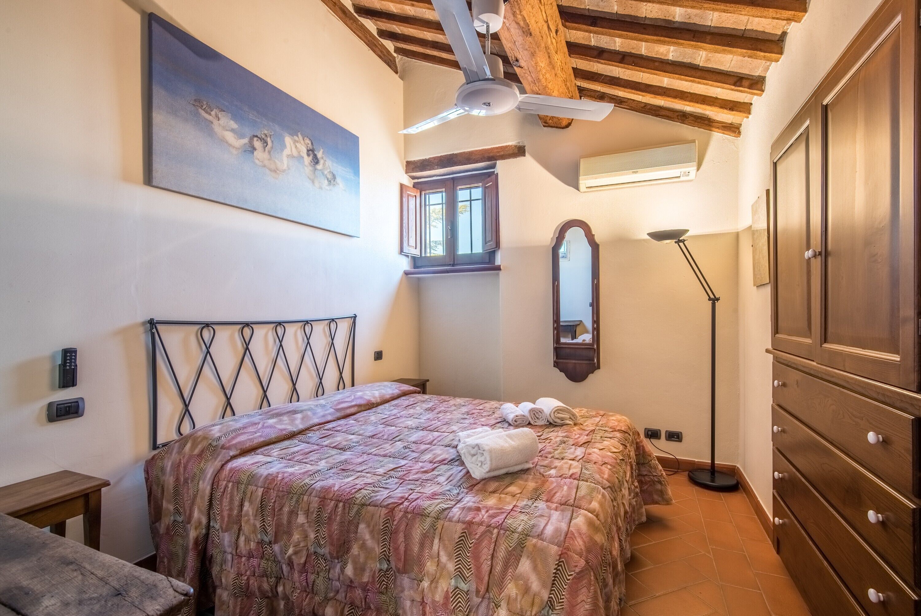 A bedroom with a bed, a ceiling fan, a window, a mirror, and a wardrobe.