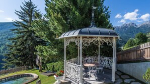 Ein Pavillon mit Glaskuppel, umgeben von einem Kiesweg, einer Holzterrasse und einem Pool.