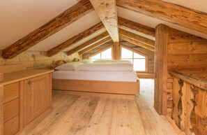 Une chambre avec un plafond en bois, un lit, une commode en bois et une fenêtre.