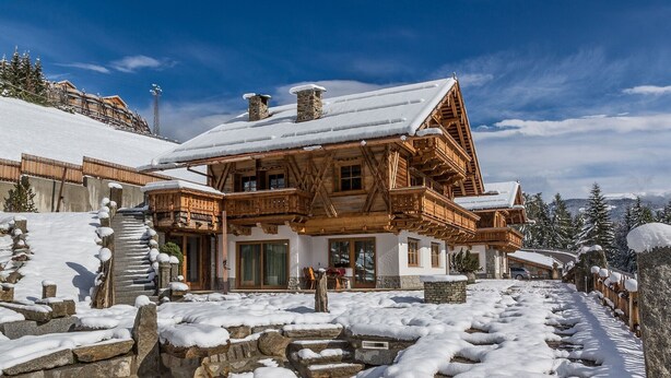 Eine Holzhütte mit schneebedecktem Dach, Steinstufen und blauem Himmel.