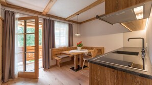 Een houten interieur met een keukenhoek, een eettafel met banken en een raam met gordijnen.