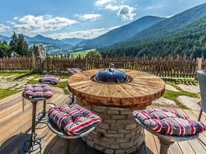 Un espace extérieur aménagé avec des sièges en bois, une table en pierre, des chaises rembourrées et une vue sur les montagnes.