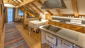 A rustic kitchen with wooden beams, a modern stove, and a dining area with a table and chairs. - Apartment Piz da Peres - Geiselsberg with Mountain View, Pool, Sauna, Wi-Fi & Garden (Olang)
