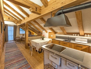 Une cuisine rustique avec des poutres en bois, un poêle moderne et un coin repas comprenant une table et des chaises.