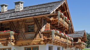 A traditional chalet with wooden balconies, stone chimneys, and a sloped roof. - Apartment Piz da Peres - Geiselsberg with Mountain View, Pool, Sauna, Wi-Fi & Garden (Olang)