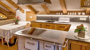 A kitchen with a central island, wooden cabinets, a built-in oven, and a hanging light fixture. - Apartment Piz da Peres - Geiselsberg with Mountain View, Pool, Sauna, Wi-Fi & Garden (Olang)