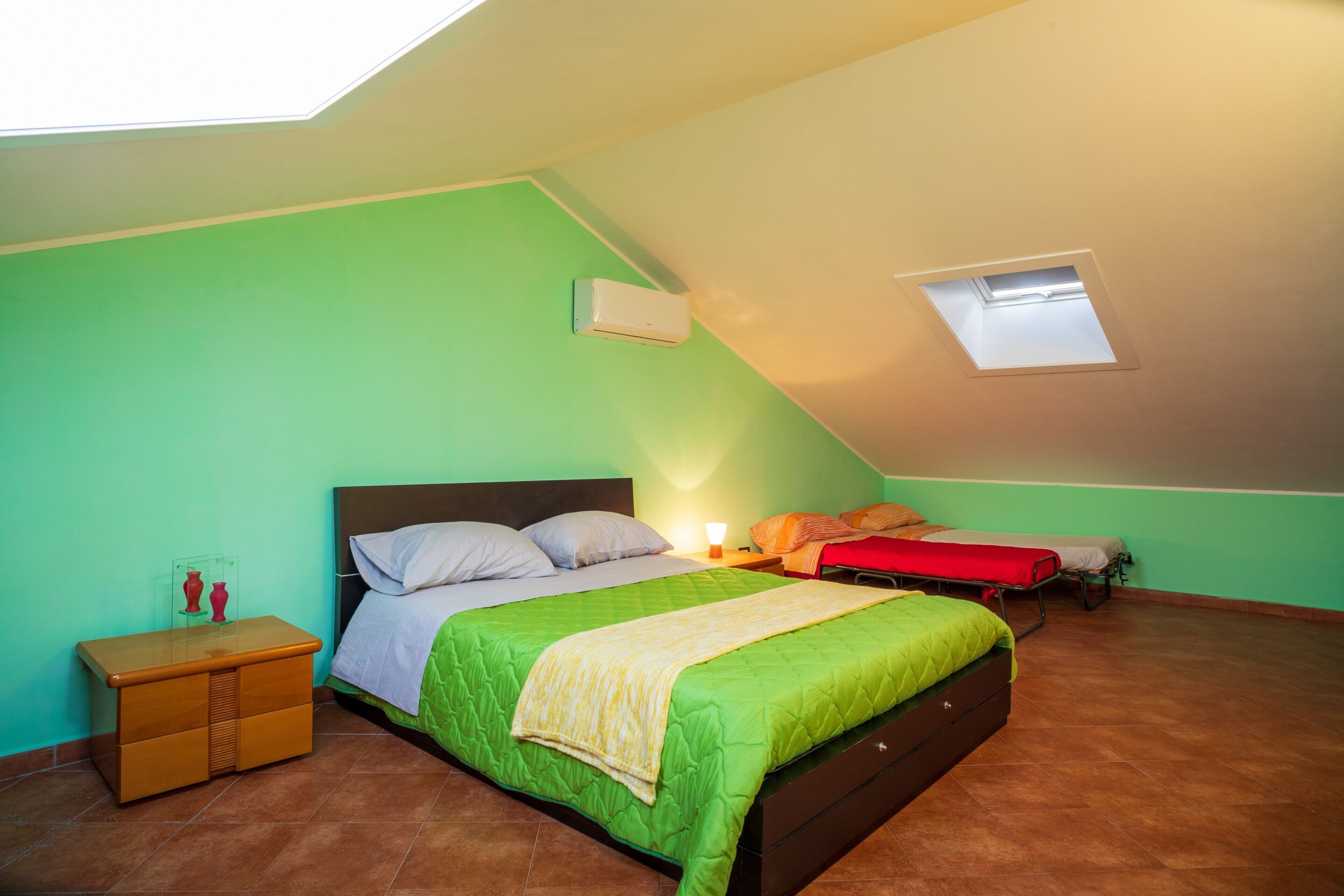 A room with a single bed, a nightstand, a dresser, a skylight, and a small window.