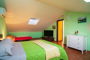 A bedroom with a green bed, a TV, a white dresser, and a skylight.