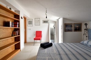 Une chambre à coucher avec un lit, une chaise rouge, une bibliothèque et une porte donnant sur une autre pièce.