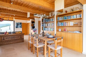 Interior de madeira com uma mesa de jantar, cadeiras, estantes de livros e vista para o exterior.