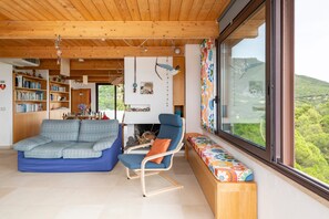 Uma sala de estar moderna com teto de madeira, um sofá, uma poltrona, estante e uma janela grande com vista.