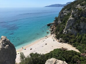 Une plage côtière bordée d’une eau turquoise et limpide, de falaises rocheuses et d’une végétation clairsemée.