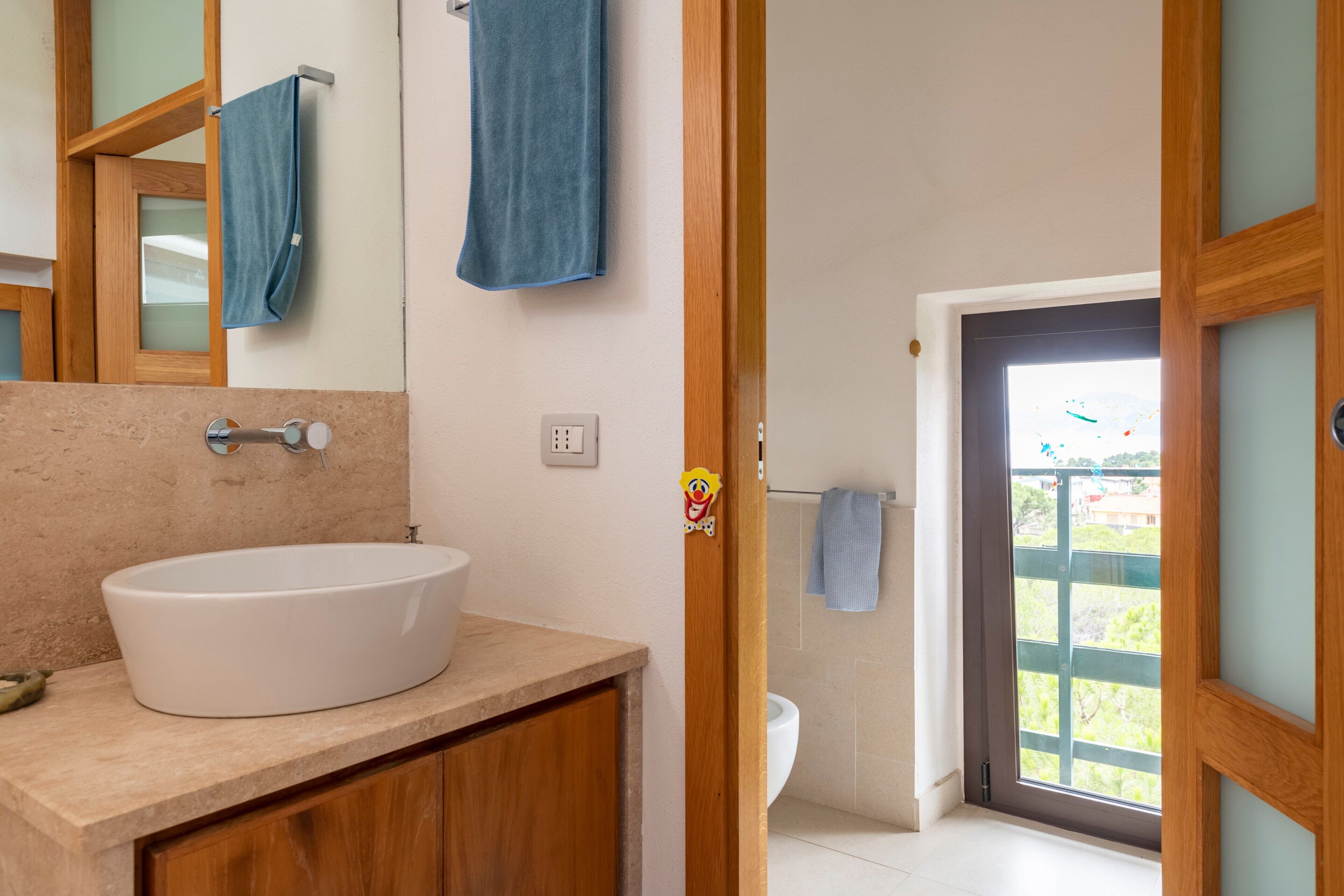 A bathroom with a white sink, wooden cabinets, a mirror, and a view through a door.