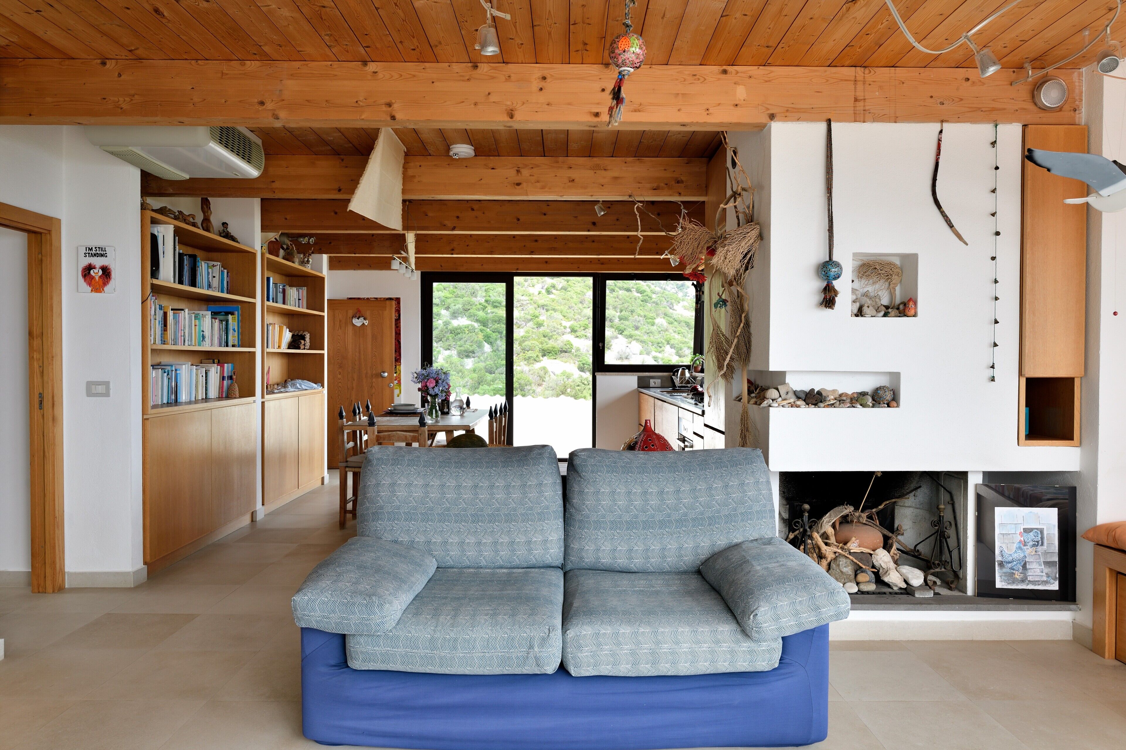 A cozy living room with a blue sofa, wooden bookshelves, a fireplace, and a large window.