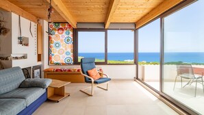 En modern inredning med ett träpanelat tak, en soffa, en fåtölj och stora fönster som erbjuder utsikt över havet.