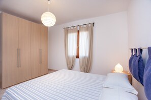 A bedroom with a bed, a wardrobe, a nightstand with a lamp, and a window with curtains.