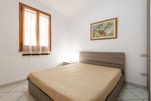 A bedroom with a bed, a nightstand, a window with curtains, and a framed picture on the wall. - Villa 'Lidia Vicino al Mare' with Mountain View, Garden & Air Conditioning (Sinnai)