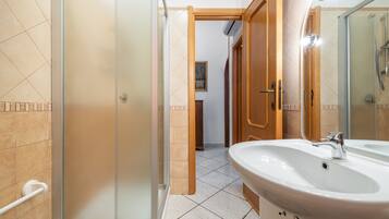 Ein Badezimmer mit Duschkabine aus Glas, einem weißen Waschbecken und einer Holztür.