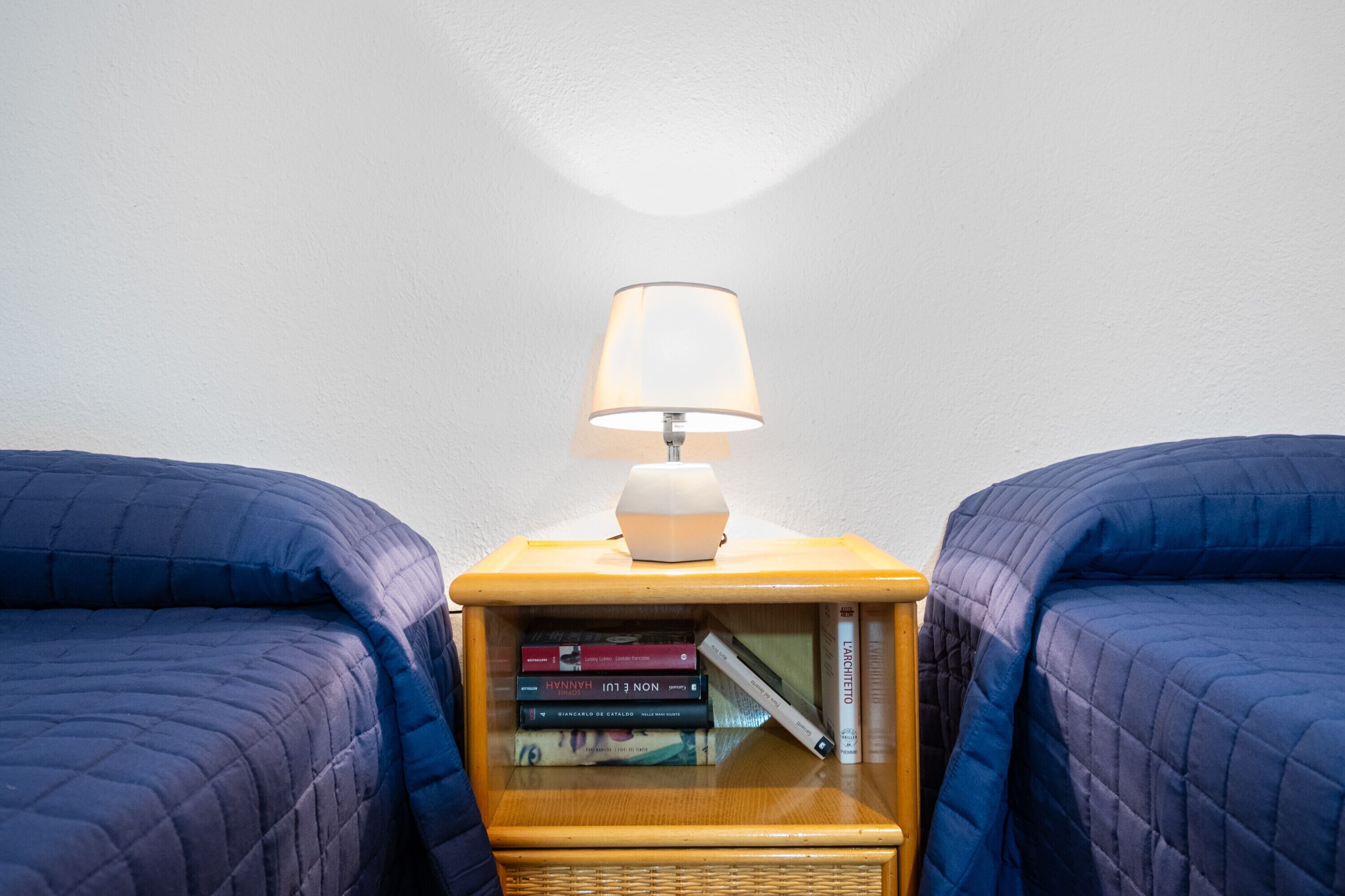Una stanza con due letti, un comodino con una lampada e una collezione di libri.