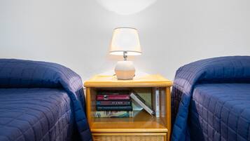 Una stanza con due letti, un comodino con una lampada e una collezione di libri.
