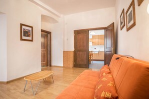 A living room with a wooden floor, a sofa, a small table, and a door leading to a kitchen. - Residence Lena  App 1 with Balcony (Pranzo)