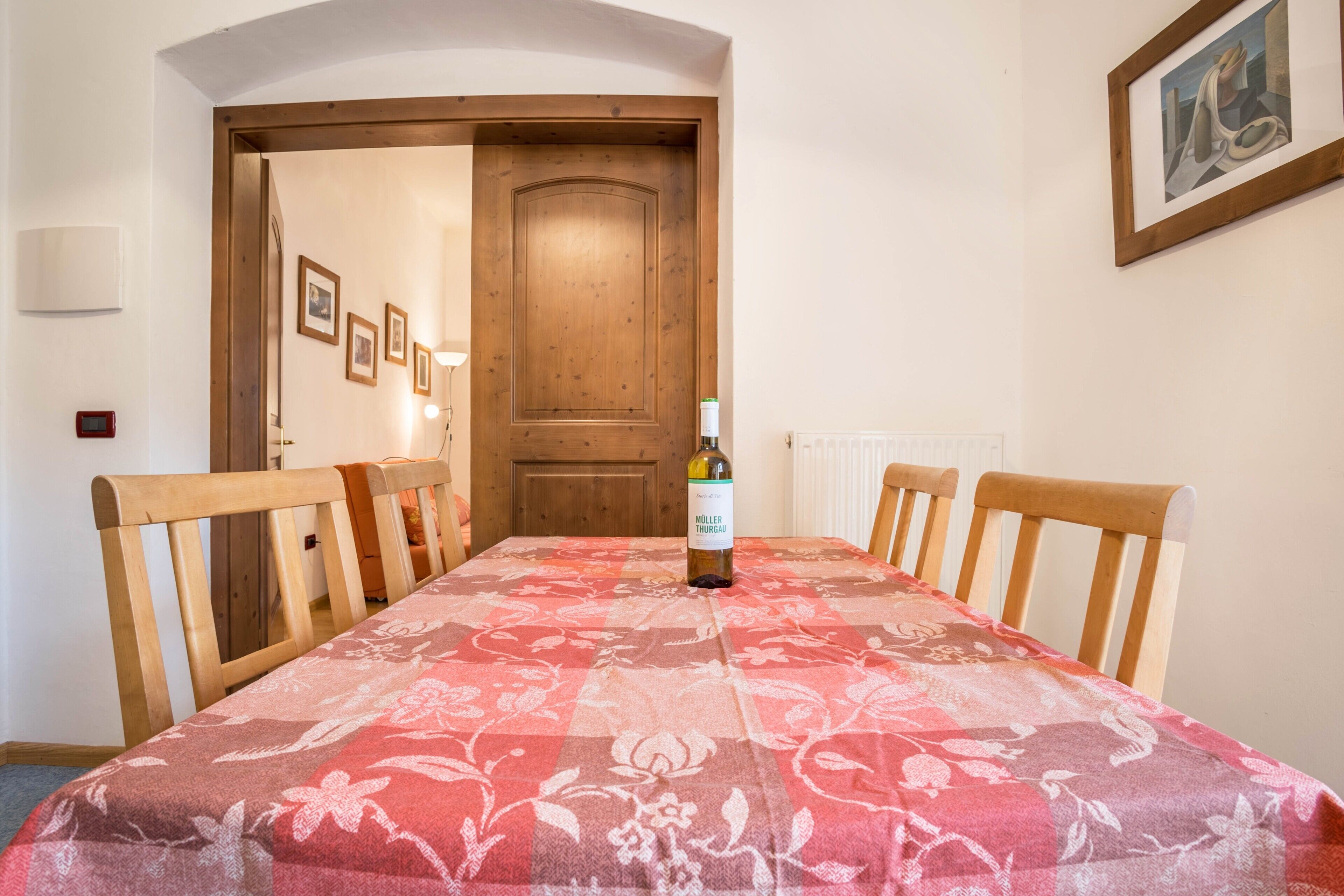 Una mesa de comedor con mantel floral, sillas de madera y una botella de vino.