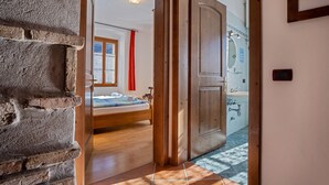 A room with a bed, a wooden door, a bathroom with a sink, and a window with a red curtain.