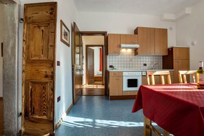 A compact kitchen with wooden cabinets, a tiled backsplash, and a red tablecloth-covered table. - Residence Lena App 2 (Pranzo)