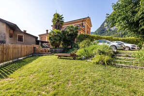 Ein Garten mit einer Holzterrasse, einem Rasen, einem Auto und einem Gebäude mit einem Glockenturm.