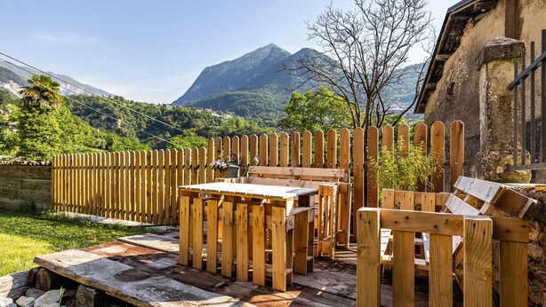 A wooden deck with a table and chairs, surrounded by a wooden fence, with a mountain in the background.