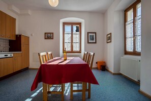 Ein Essbereich mit einem für sechs Personen gedeckten Tisch, einem Fenster mit Vorhängen, Holzschränken und einer Heizung.