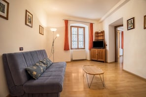 Un salon comprenant un canapé, un fauteuil en osier, un radiateur, un téléviseur et un meuble en bois.