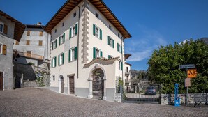 Un bâtiment doté d’une façade en pierre, de nombreuses fenêtres avec volets et d’une entrée imposante surmontée d’une arche.