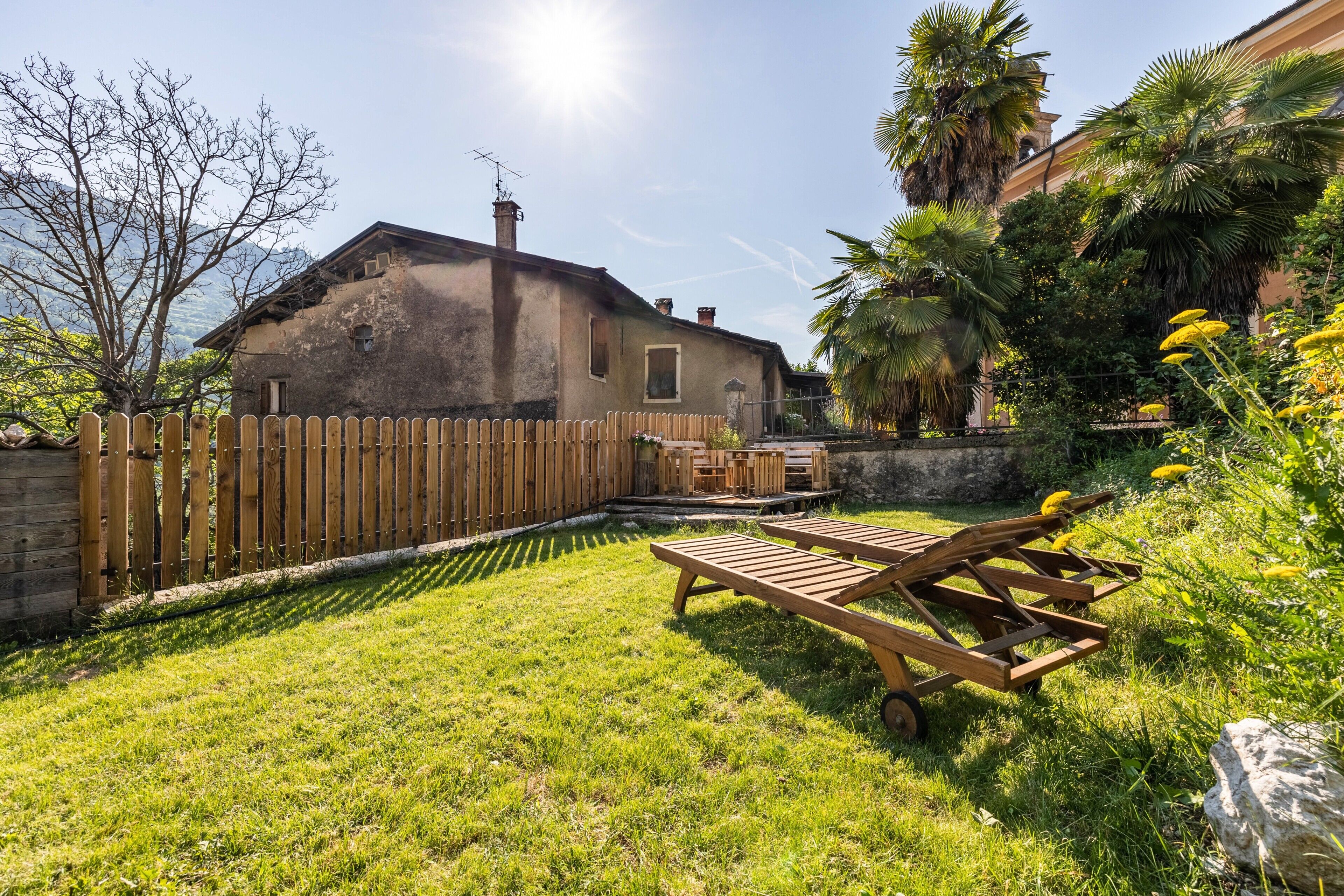 Ein Garten mit Holzzaun, einer Holzdielenterrasse und einem Haus mit Schornstein.