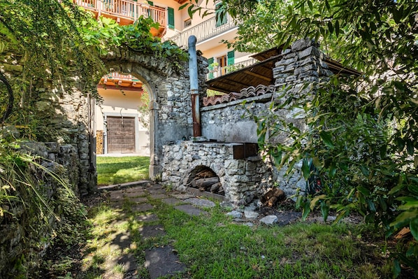 Un arco de piedra que da acceso a un edificio con una escalera de madera y un muro de piedra con chimenea.