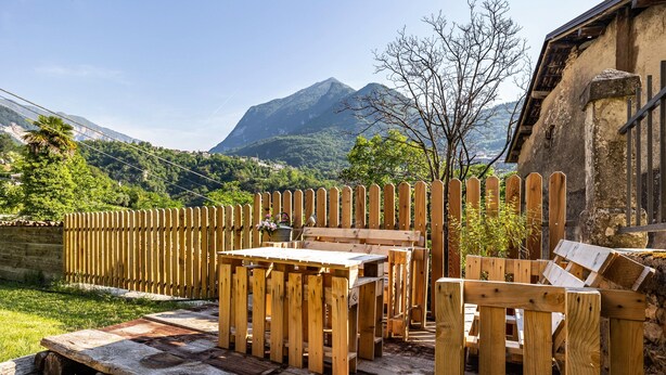 Une terrasse en bois avec une table et des chaises, entourée d’une clôture en bois, et une montagne en arrière-plan.
