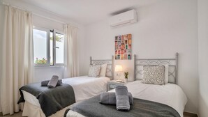 A hotel room with two beds, a nightstand, a lamp, a wall-mounted air conditioner, and a window with curtains. - Holiday Home "Alegria" close to the Beach with Garden & Wi-Fi (Puerto del Carmen)