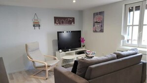 Un salon avec un canapé, un fauteuil, un téléviseur et une petite table sur laquelle est posé un vase de fleurs.
