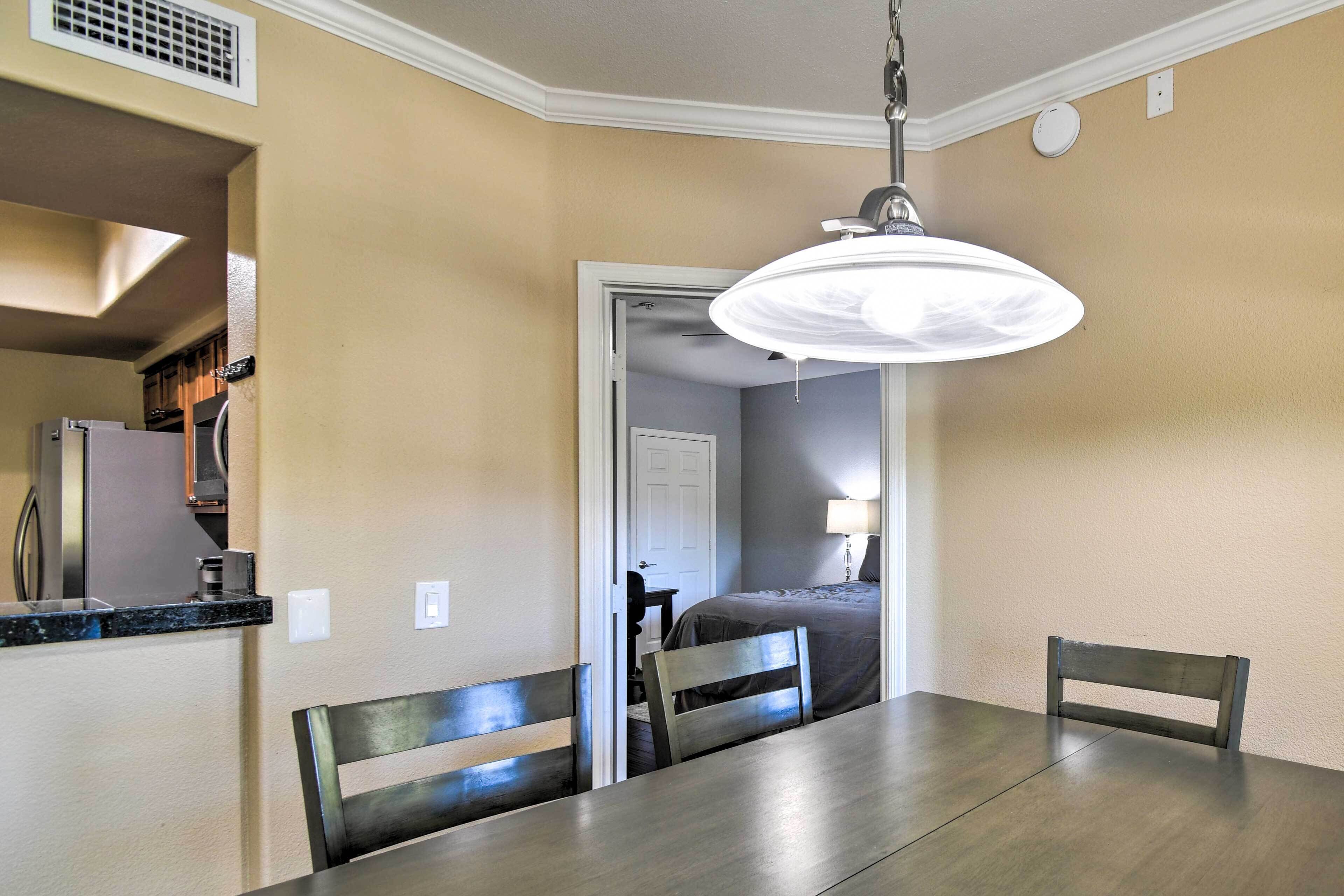 A dining area with a table, chairs, a ceiling light fixture, and a kitchen in the background.